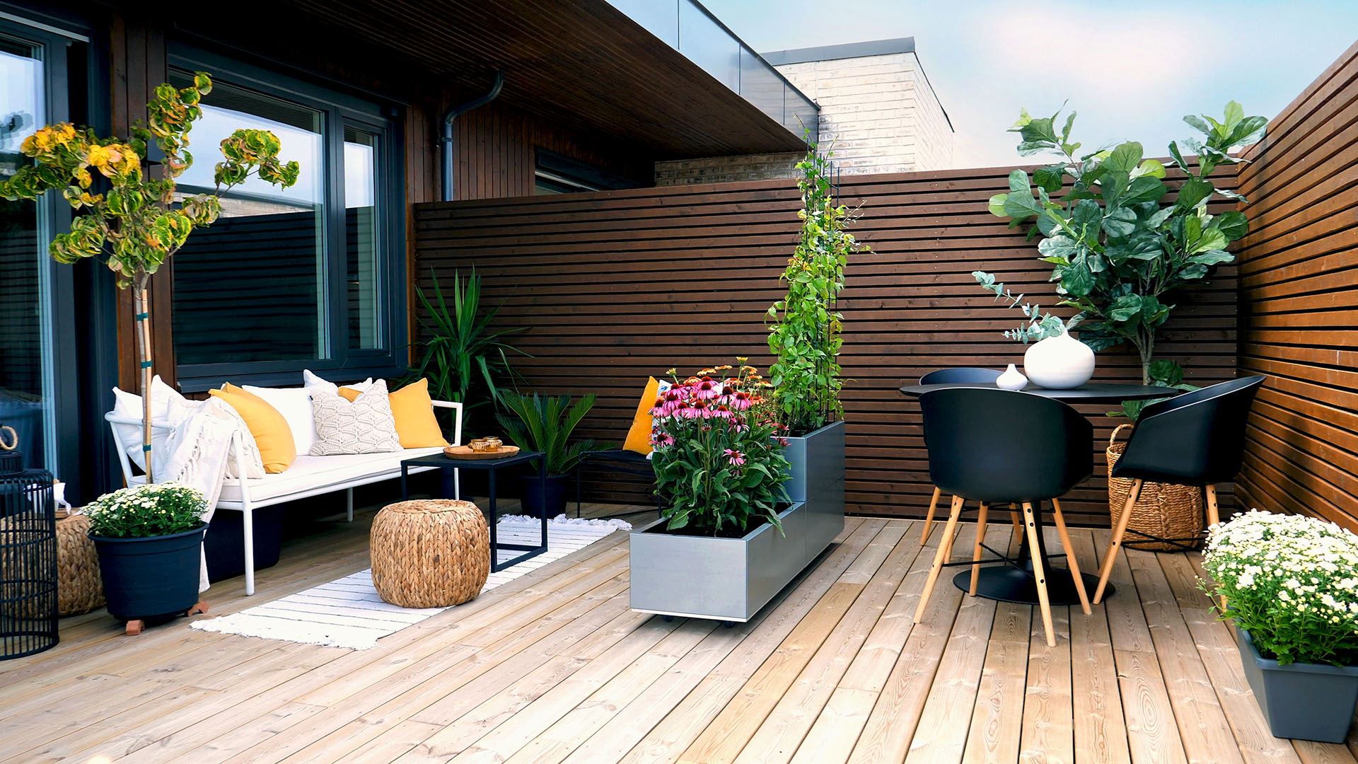 Oversiktsbilde av balkong med sittegruppe, store planter i krukker og kar og spisegruppe. Foto.